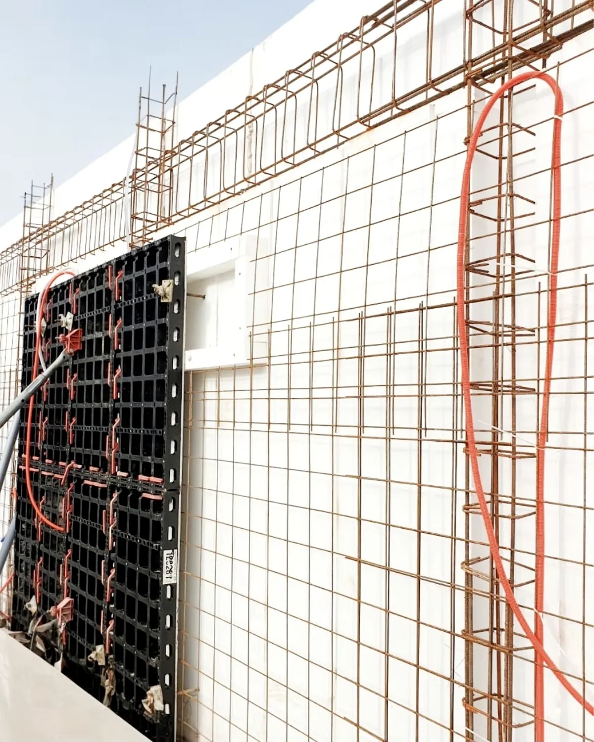 Construction photograph of a reinforced-concrete wall assembly before the pour: continuous reinforcement mesh and vertical reinforcing cages across the insulated core.
